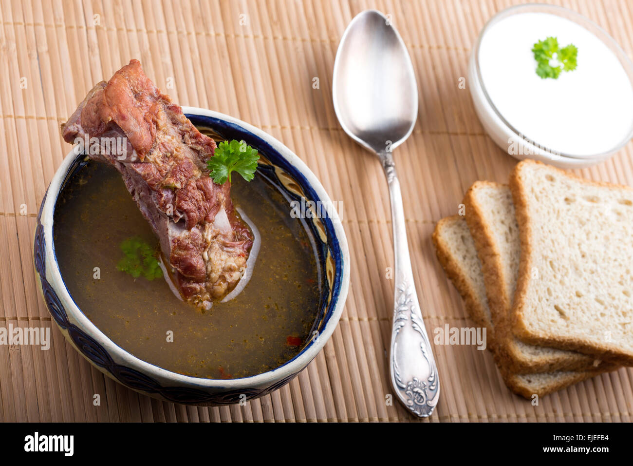 Gemüsesuppe mit geräuchertem Fleisch, Brot, Creme und silberne Löffel auf hölzernen Tischdecke Stockfoto