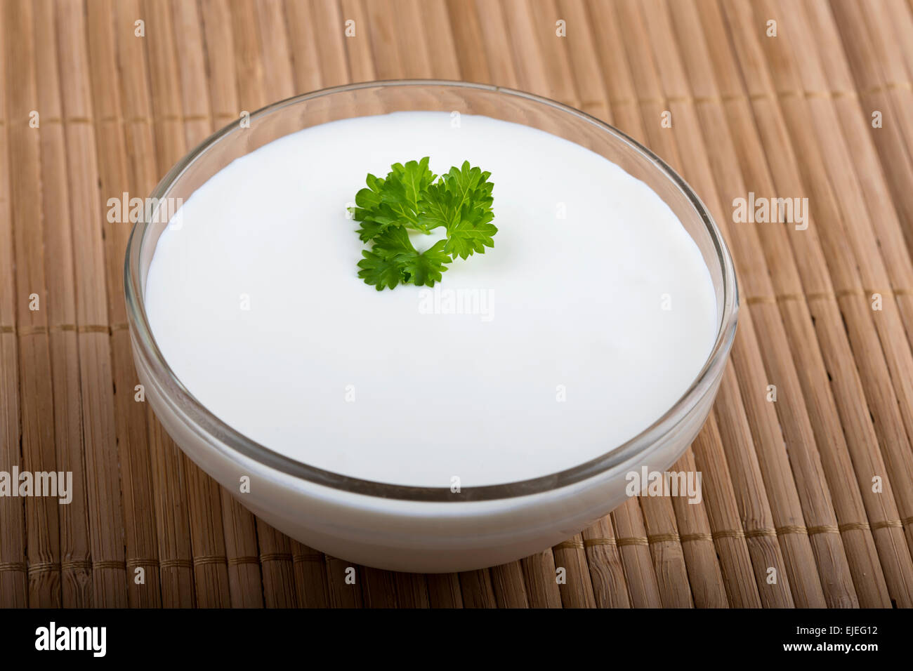 Schüssel saure Sahne mit einem Blatt Petersilie auf hölzernen Tischdecke Stockfoto