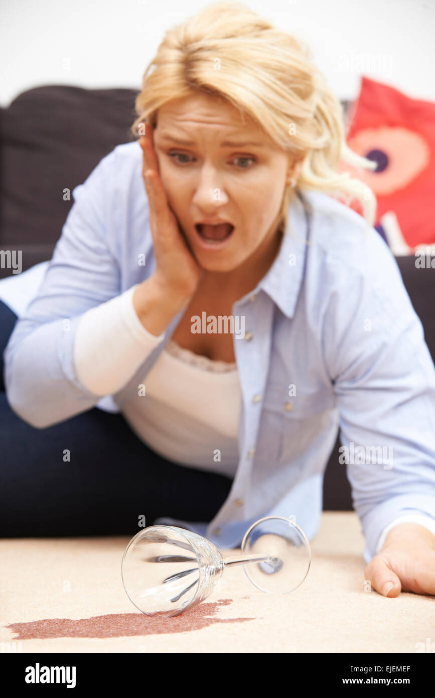 Frau versehentlich verschüttet Rotwein auf Teppich zu Hause Stockfoto