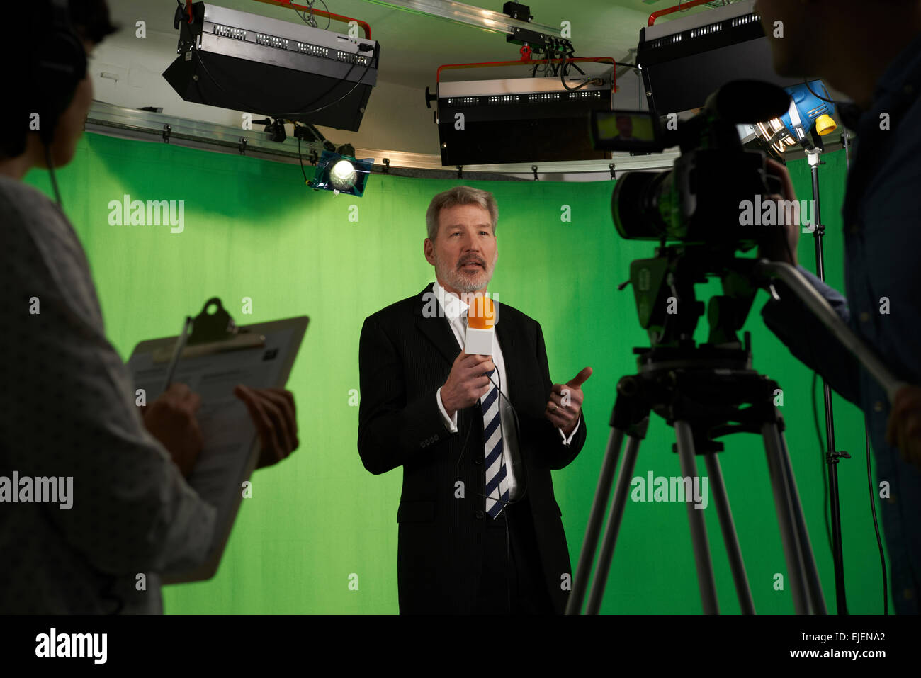 Männliche Moderatorin im Fernsehen Stdio mit Crew im Vordergrund Stockfoto