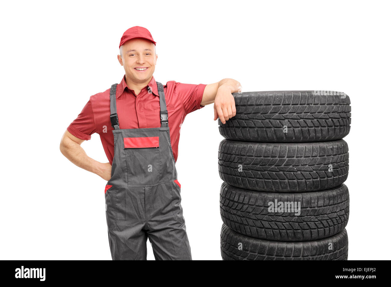 Männliche Mechaniker in ein rotes Hemd und grauen Overall stützte sich auf einen Stapel von Reifen isoliert auf weißem Hintergrund Stockfoto