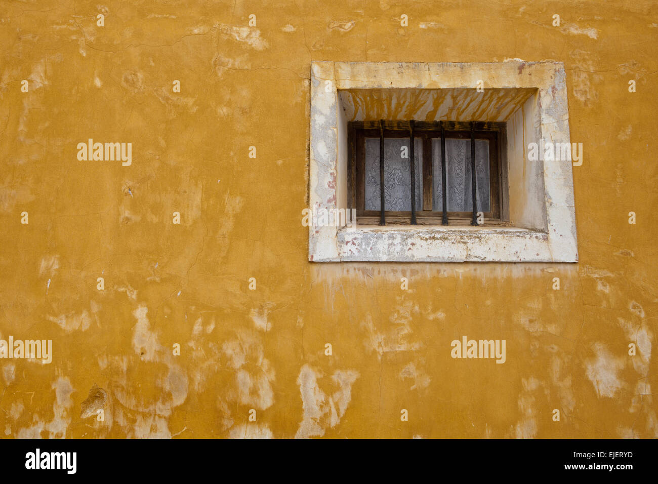 Alte gelbe Wand mit kleinen Fenster mit weißen häkeln Haken Duschabtrennung, Pastrana, Spanien Stockfoto