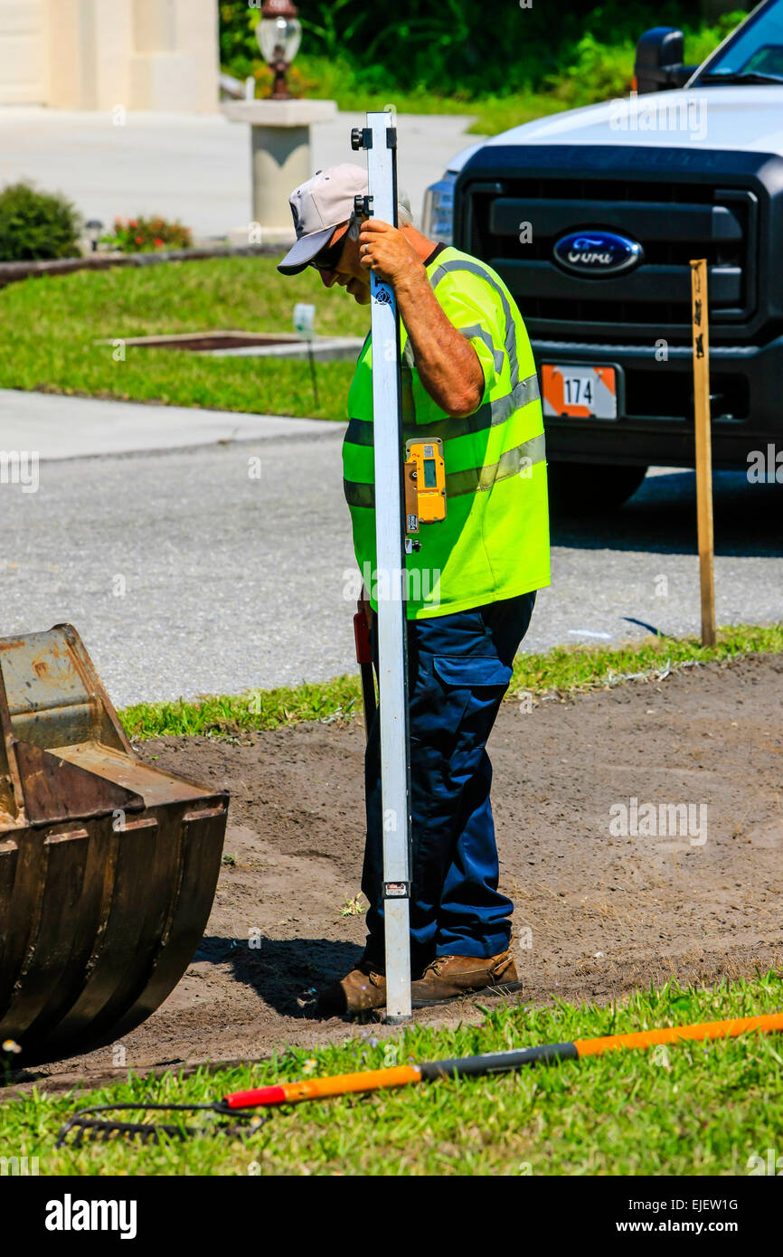 Autobahn Wartung Worker mit einem digitalen Tiefe Guage als Bagger entfernt Boden als Bestandteil der Regenwasserabfuhr einweichen entfernt Stockfoto