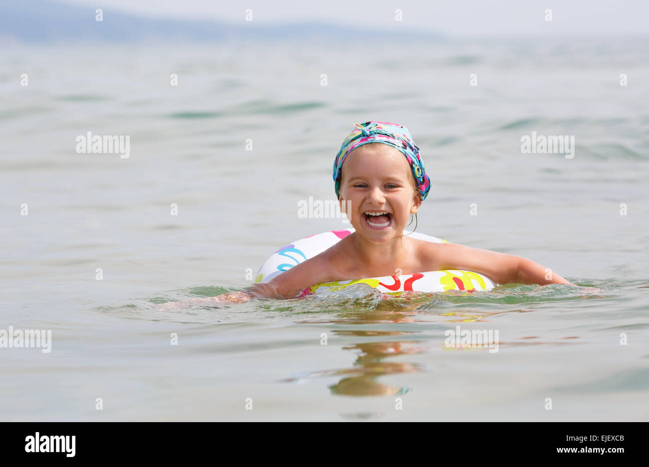 Glückliches Kind schwimmt im Meer auf aufblasbaren Ring an einem klaren sonnigen Tag. Geringe Schärfentiefe. Modell im Mittelpunkt. Stockfoto