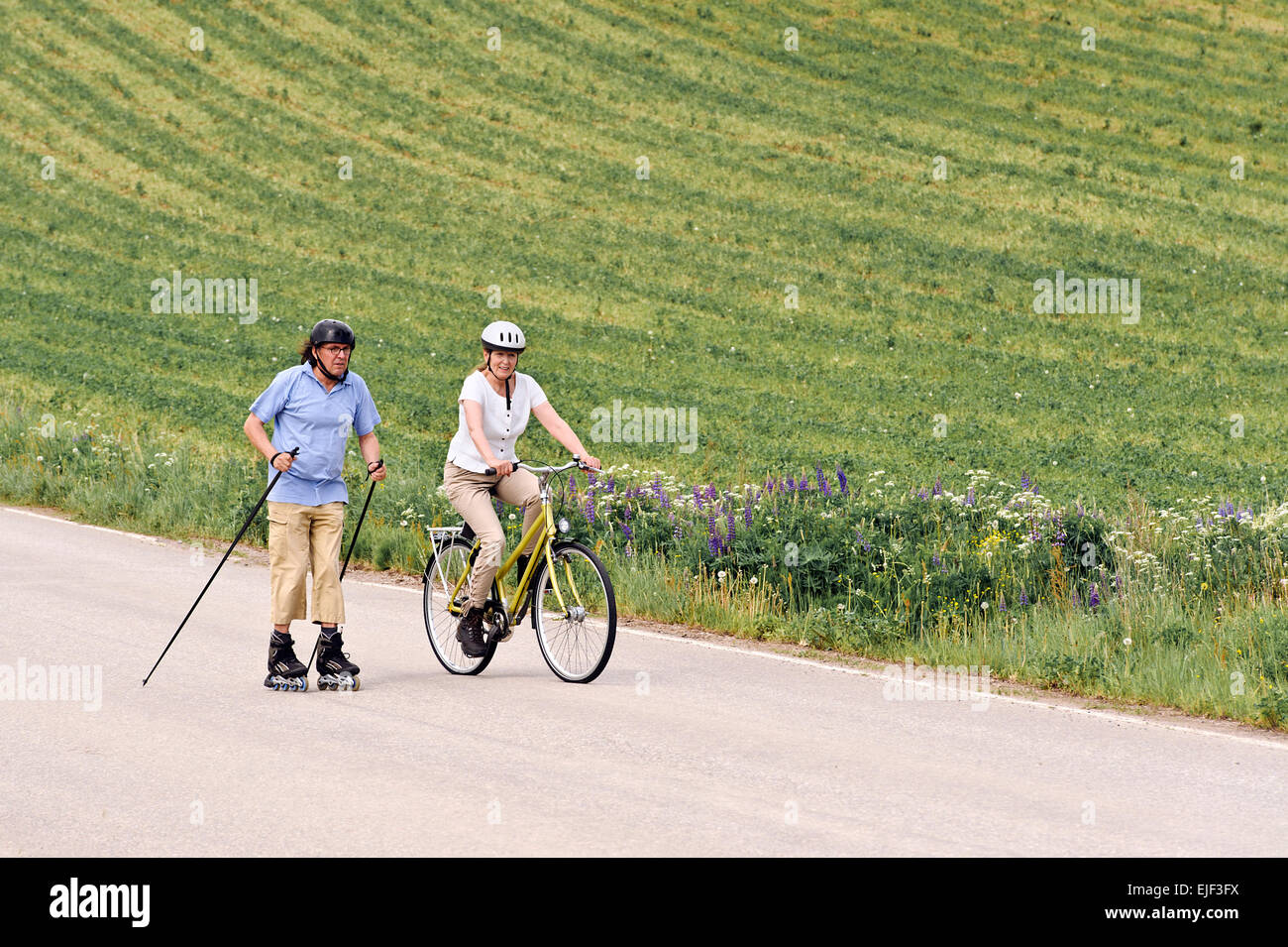 Älteres paar kräftig trainieren. Der Mann ist Nordic Inline-skating, und die Frau ist das Radfahren. Sie sind auf einem Land Straße throu Stockfoto