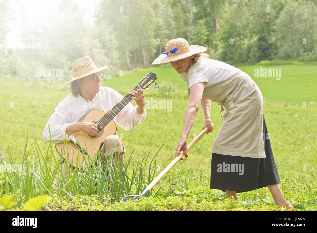 Ältere Mann und Frau in einem Gemüsegarten. Die Frau ist den Boden Rechen. Der Mann ist eine Gitarre spielen. Stockfoto