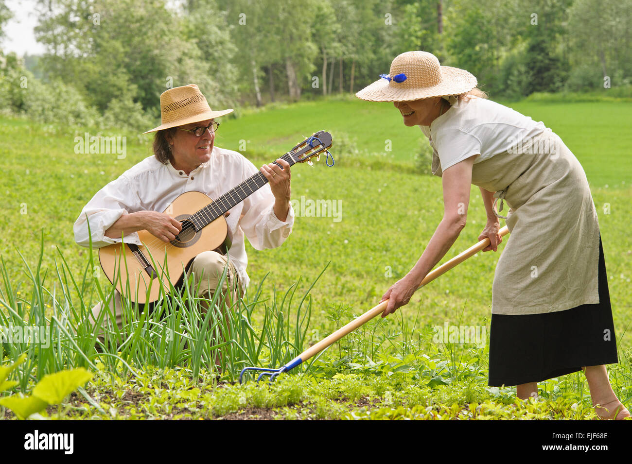 Ältere Mann und Frau in einem Gemüsegarten. Die Frau ist den Boden Rechen. Der Mann spielt Gitarre Stockfoto