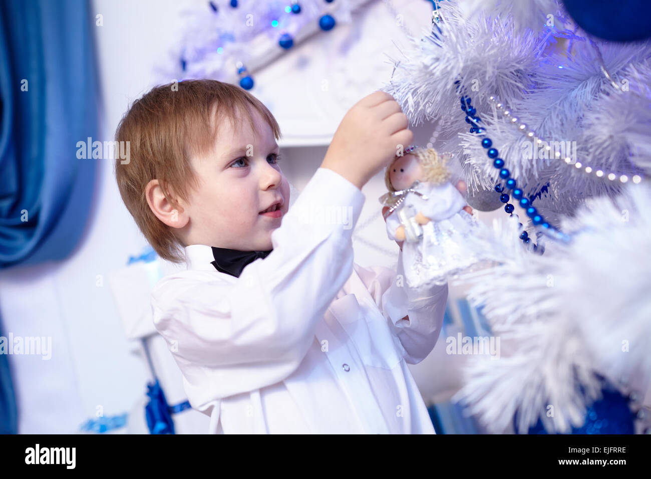 kleiner Junge in ein weißes Hemd und Fliege schmückt einen Weihnachtsbaum Stockfoto