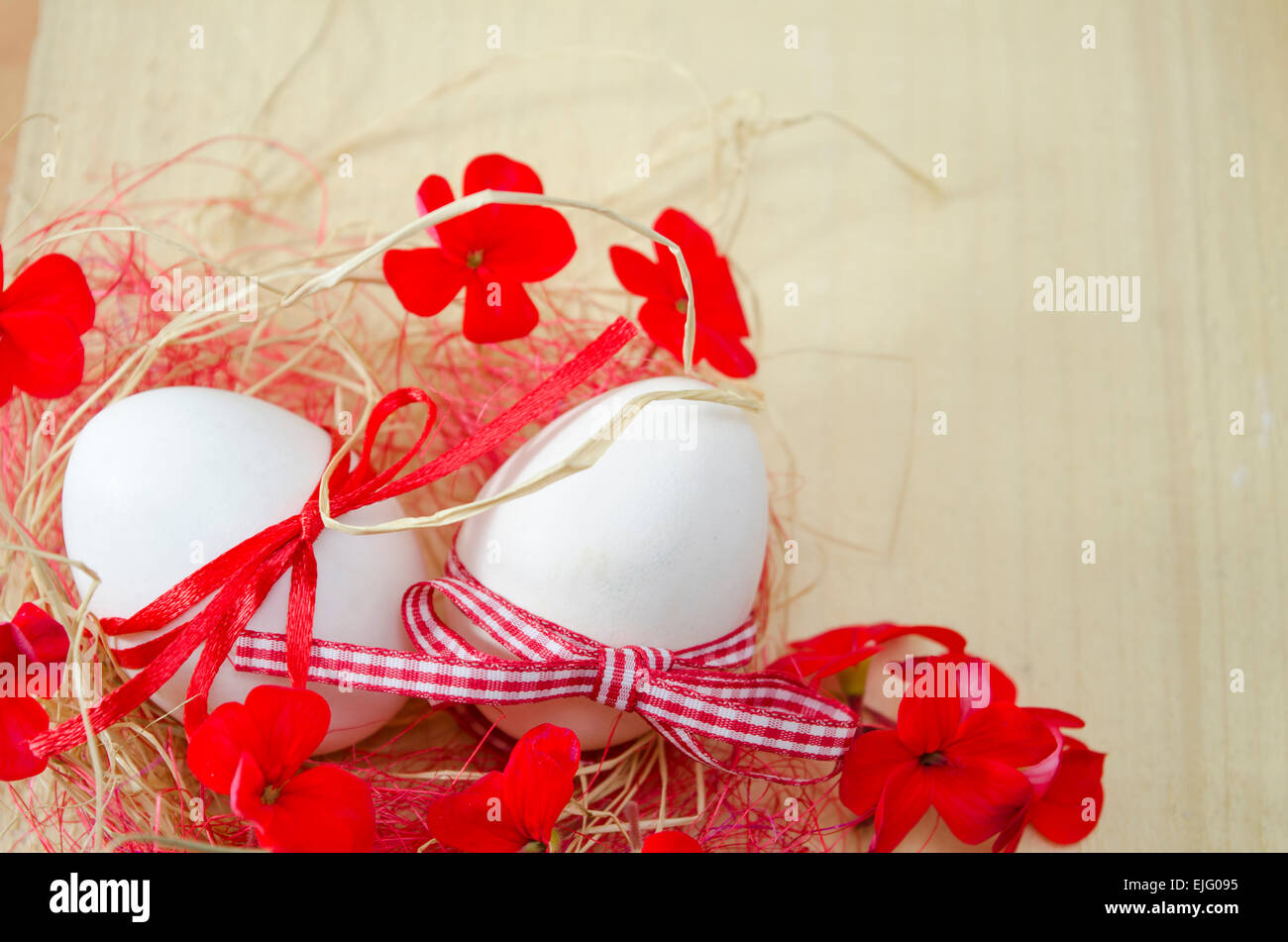 Zwei weißen Eiern mit Bändern befestigt, liegend in einem Nest mit zwei roten Blüten Stockfoto