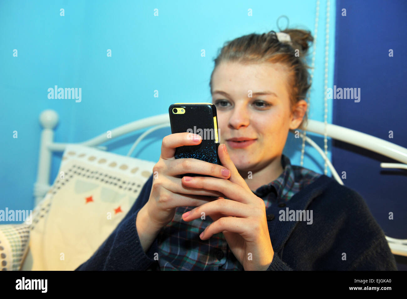 Teenager-Mädchen prüft Facebook und Twitter auf ihrem Mobiltelefon in ihrem Schlafzimmer Stockfoto