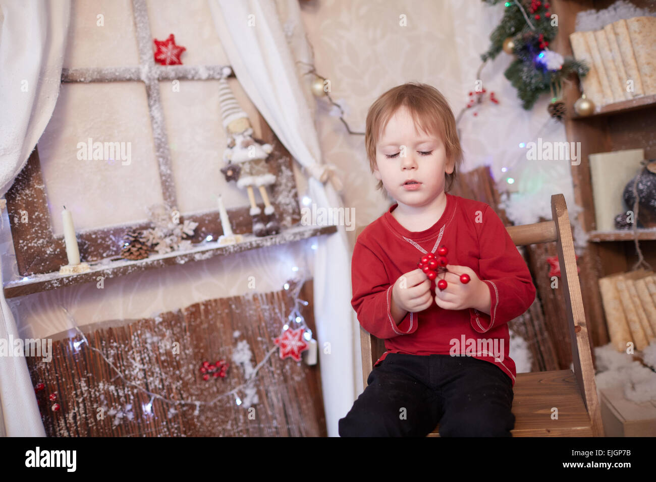 Boy fünf Jahre in Vorfreude auf den Urlaub, in der Nähe der Weihnachtsbaum sitzen hält eine Reihe von roten Beeren Stockfoto