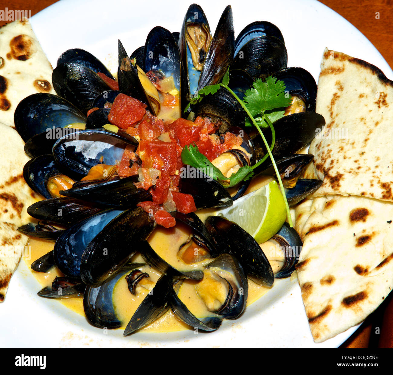 Gedämpfte Muscheln Kokos Currysoße gehackte gekochte Tomaten Pita Brot Keile Stockfoto