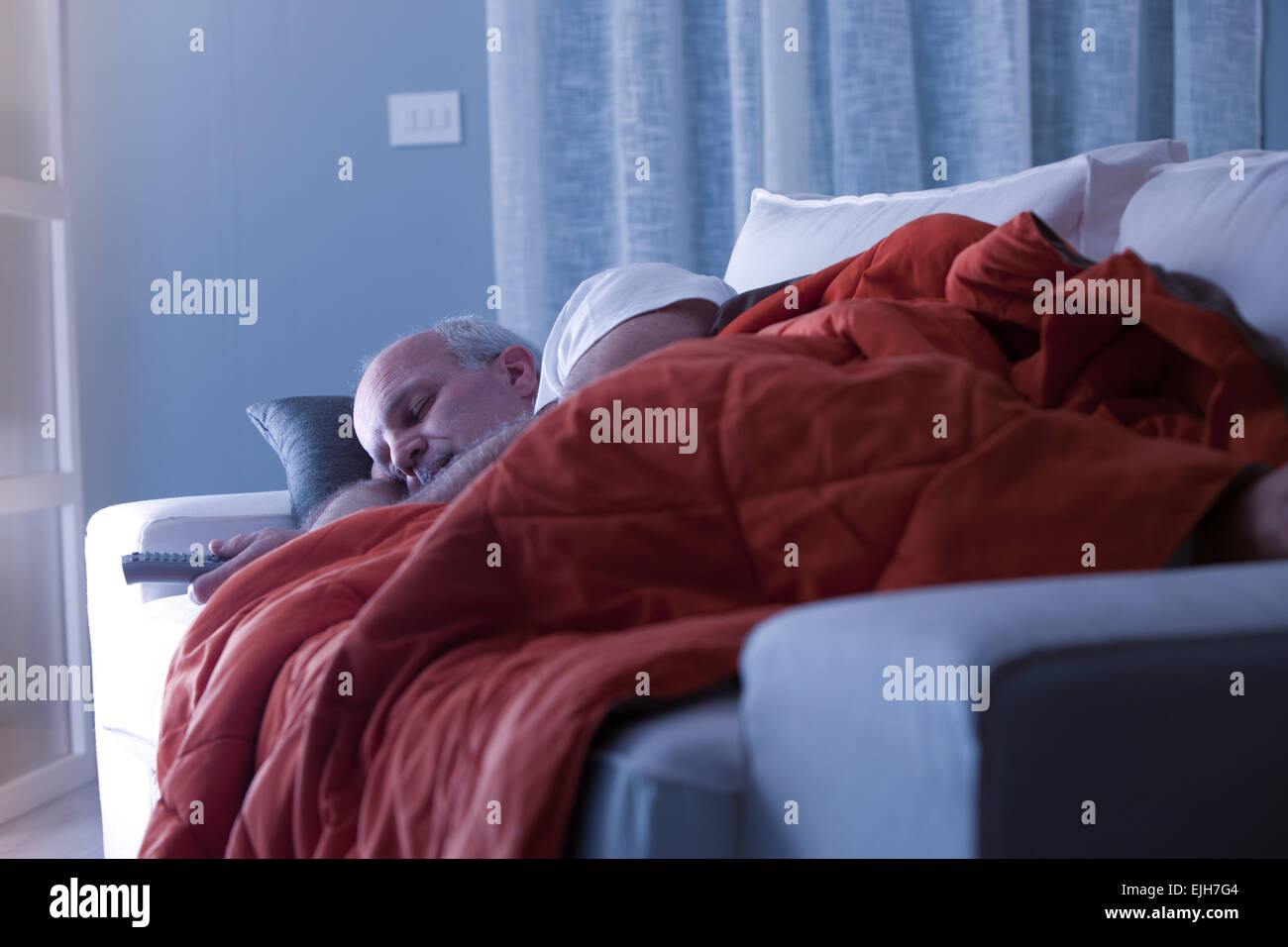 Mann schläft auf seiner Couch in einem weißen Wohnzimmer Stockfoto