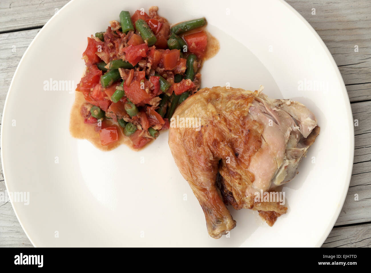 Brathähnchen Sie mit sautierten grünen Bohnen und Tomaten auf einem weißen Teller auf einem rustikalen Tisch sitzen. Stockfoto