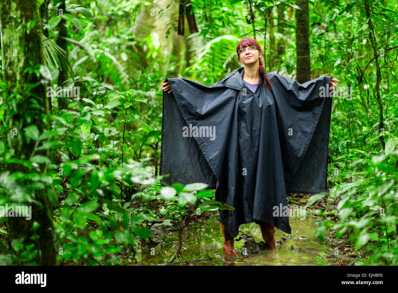 Touristische Frau in Amazonas Dschungel zeigt typische Ausrüstung und Bekleidung für diese Umgebungen Regenponcho und Gummistiefel Stockfoto
