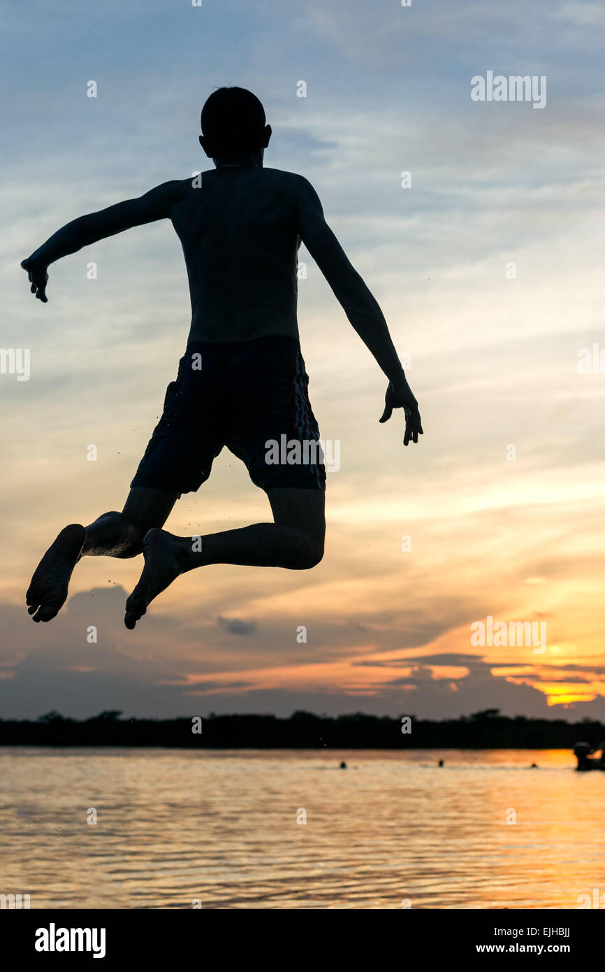 Erwachsener Mann springt in den See gegen Sonnenuntergang Stockfoto