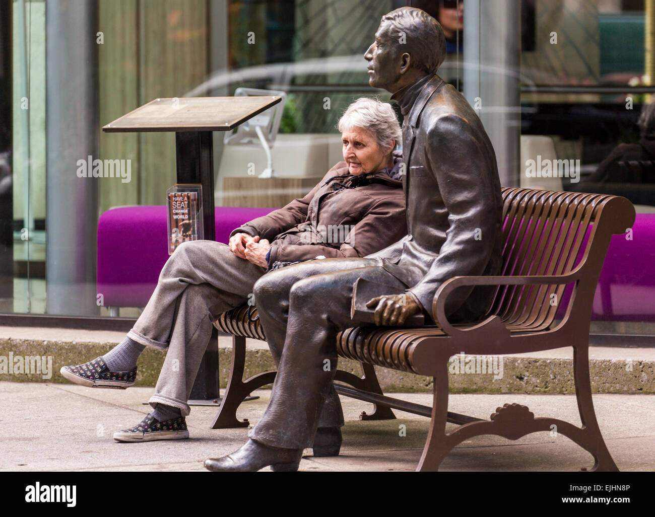 Frau sitzt auf der Bank neben Bronze Statue eines Mannes, New York City, USA Stockfoto