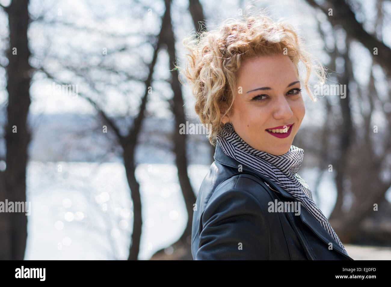 Porträt einer hübschen jungen Frau mit blonden lockigen Haaren lächelnd und verschwinden im Wald am Fluss Stockfoto