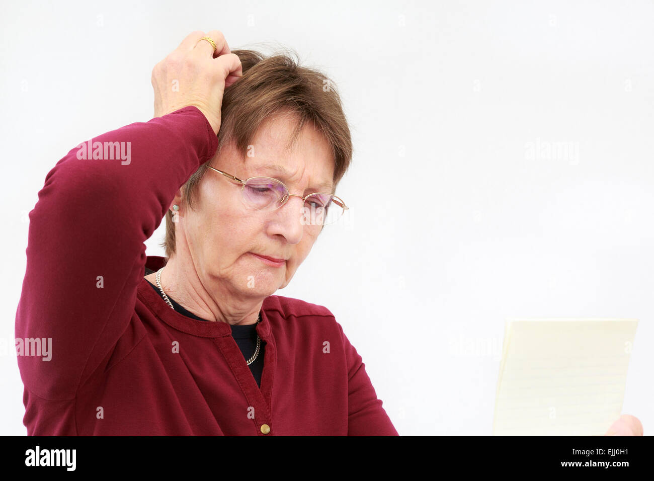 Ein besorgter älterer Frau Kratzer den Kopf beim Lesen ein verwirrendes schreiben Sie hält und Denken. England, Großbritannien, Großbritannien Stockfoto