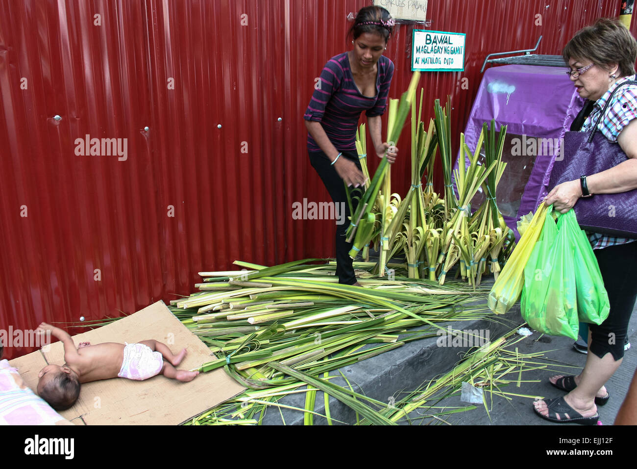 Manila, Philippinen. 27. März 2015. Ein Palm Frond Verkäufer in Quiapo verkauft ein Bündel an einem Käufer, während ihr Baby aus einem Mittagsschlaf erwacht. Kostet ca. 40 US-Cent je Verkäufer Ansturm auf ihre Palmwedel bereiten Sie ein paar Tage vor dem Palmsonntag. Bildnachweis: Pazifische Presse/Alamy Live-Nachrichten Stockfoto