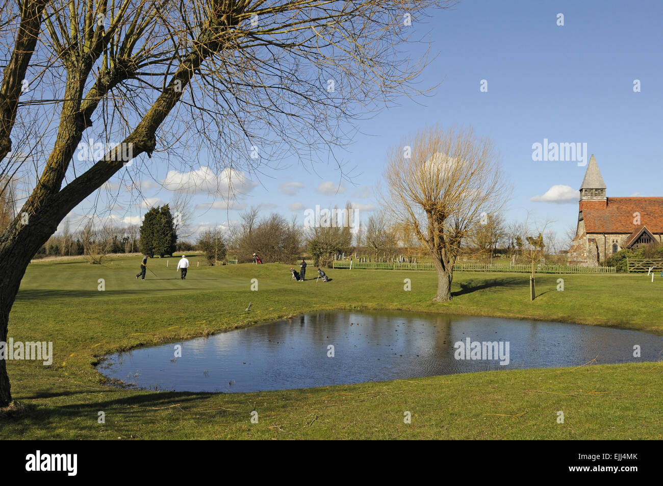 Blick über den Teich auf dem 1. Loch auf dem Grün und eine kleine Kirche Burnham-auf-Crouch Golf Club Essex England Stockfoto