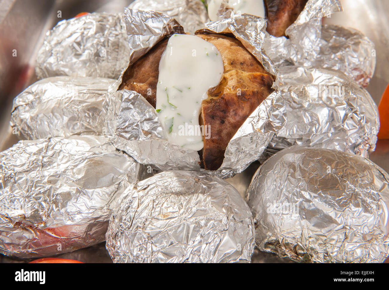 Nahaufnahme der gebackene Pellkartoffeln in Silber Metallfolie mit weißer Soße in einem Hotel-Restaurant-buffet Stockfoto