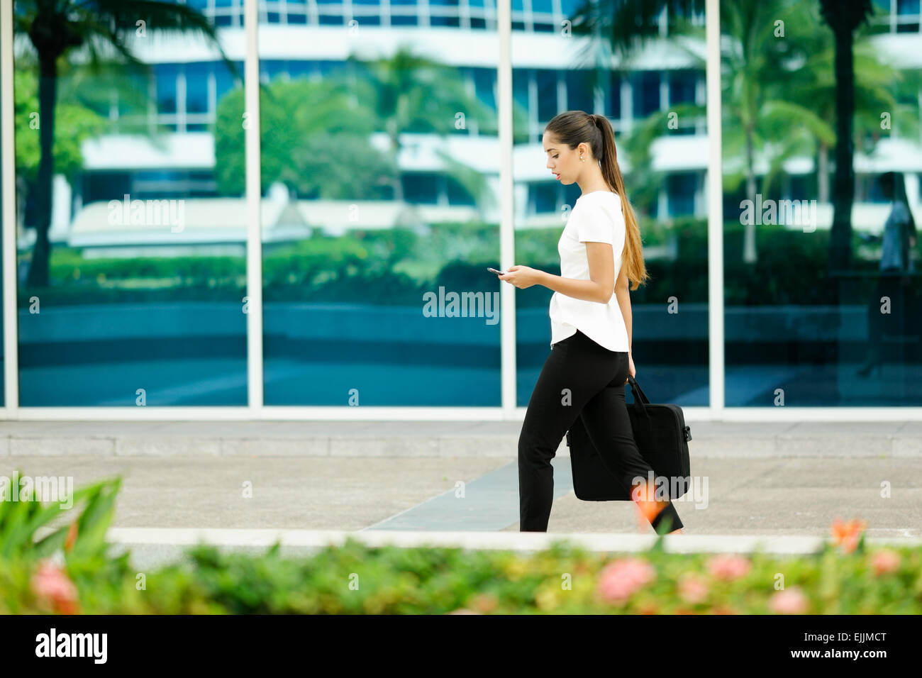 Blick auf Business-Frau zu Fuß in die Stadt Straße mit Laptop-Tasche, im Chat auf Handy und gehen morgens zur Arbeit beschnitten Stockfoto
