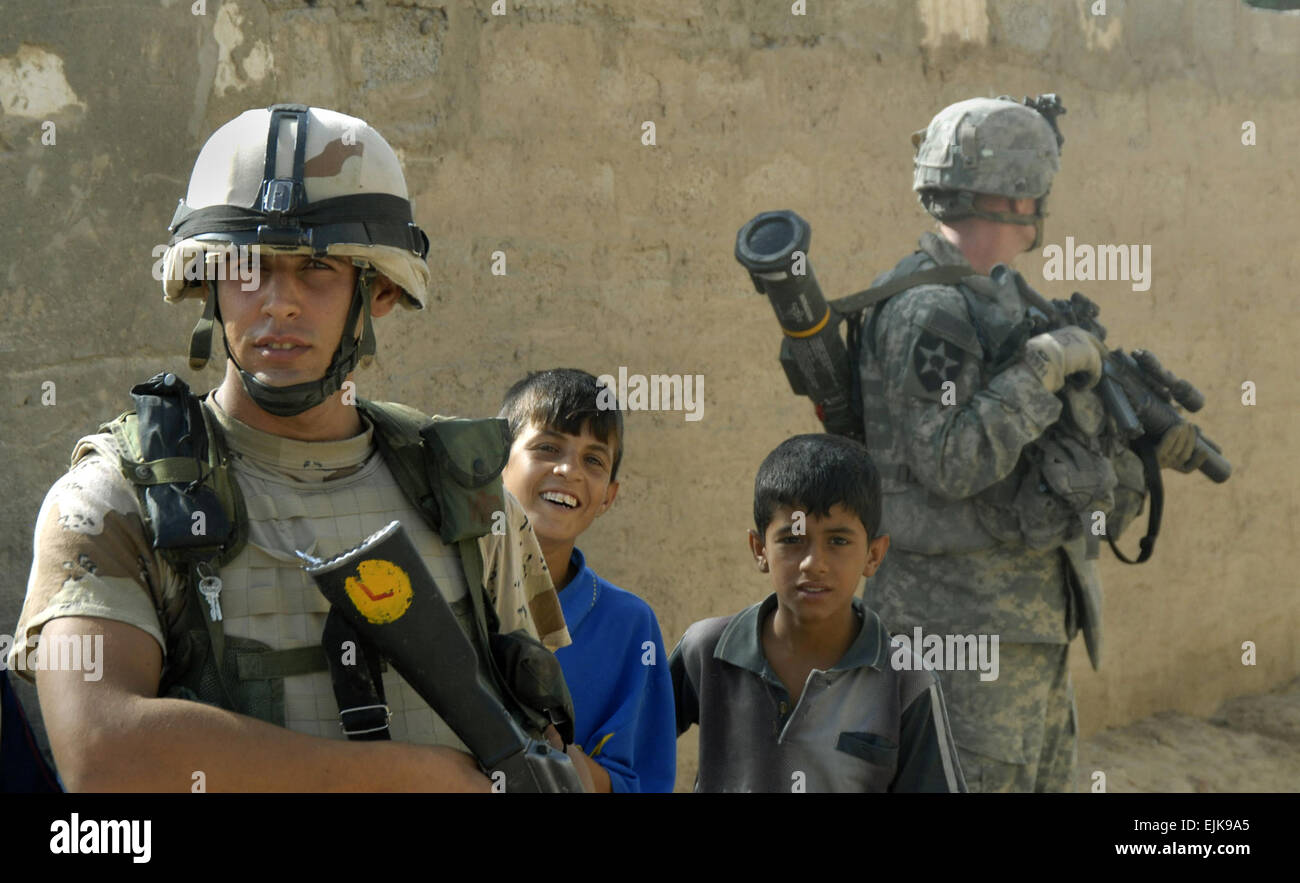 Eine irakische Armee Soldat ist flankiert von zwei jungen, wie ein Soldat der US Armee zugewiesen an Alpha Batterie Sicherheit während einer gemeinsamen Mission in Khan Bani Sa'ad, Irak, 12. Juli 2007 bietet.  Soldaten aus Alpha-Batterie, 2. Bataillon, 12. Feldartillerie-Regiment, 4. Stryker Brigade Combat Team, 2. US-Infanteriedivision und Einheiten der irakischen Armee führen einen Kordon und Mission in Bereich der Aufständischen zu löschen und cache-Seiten zu suchen.  Masse der Kommunikationsspezialist 2. Klasse Scott Taylor Stockfoto