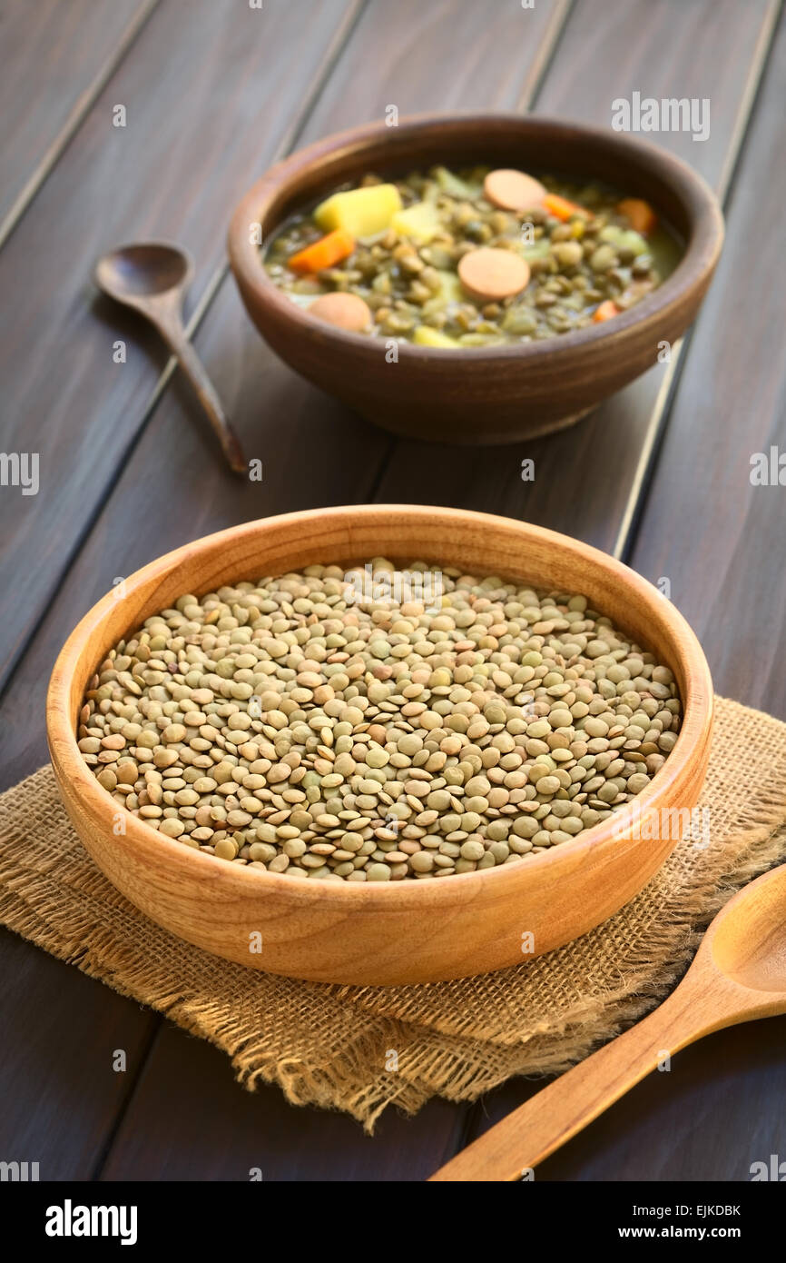 Rohe Linsen (lat. Lens Culinaris) in Holzschale mit einer rustikalen Schüssel Linsensuppe (mit Linsen, Karotten, Kartoffeln, Wurst gemacht) Stockfoto