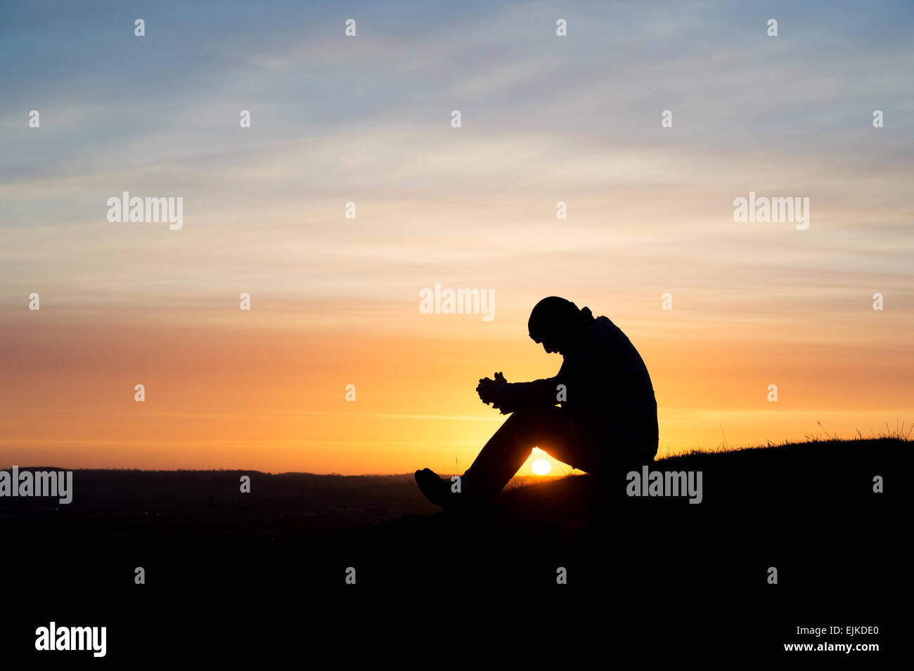 Nachdenklicher Mann sitzt auf einem Hügel bei Sonnenaufgang. Silhouette Stockfoto
