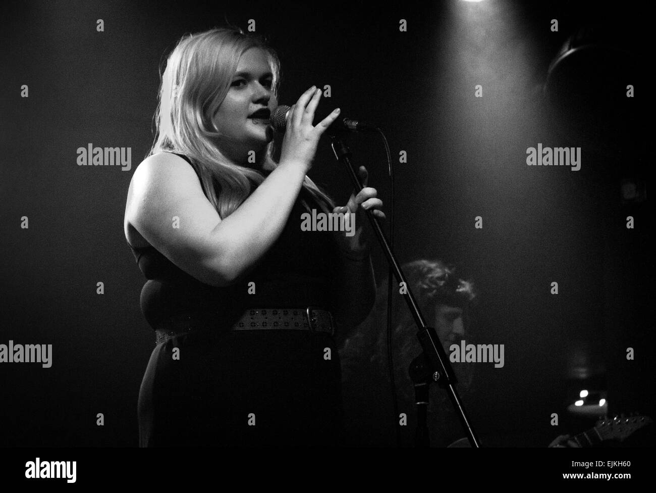 Frau mit blonden, lange, glatte Haare Gesang in ein Mikrofon, während Sie den Ständer in einer Band zu halten. Stockfoto