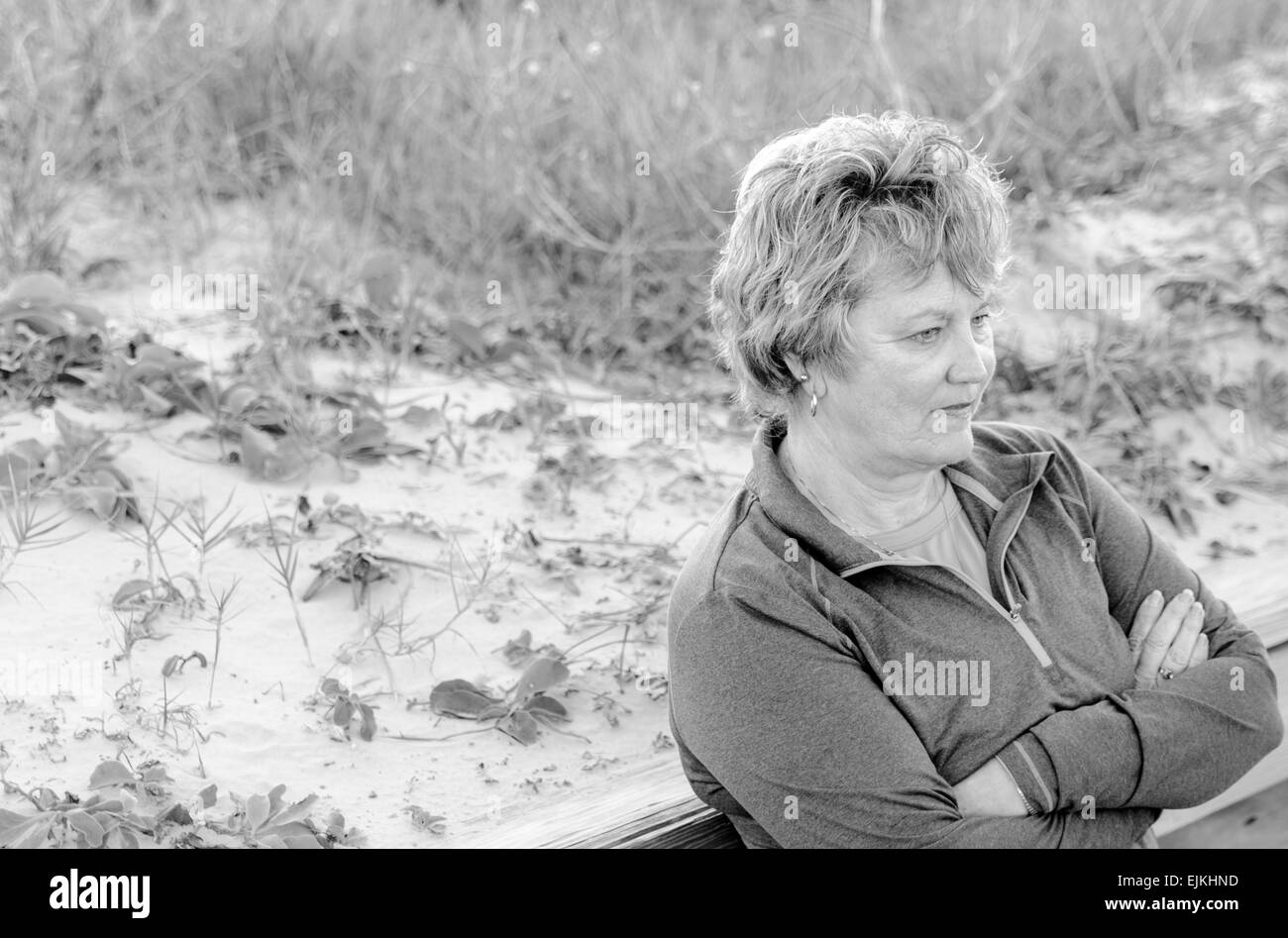 Ältere Frau entspannt warten beim schiefen gegen ein Geländer in Strandnähe in schwarz / weiß Stockfoto