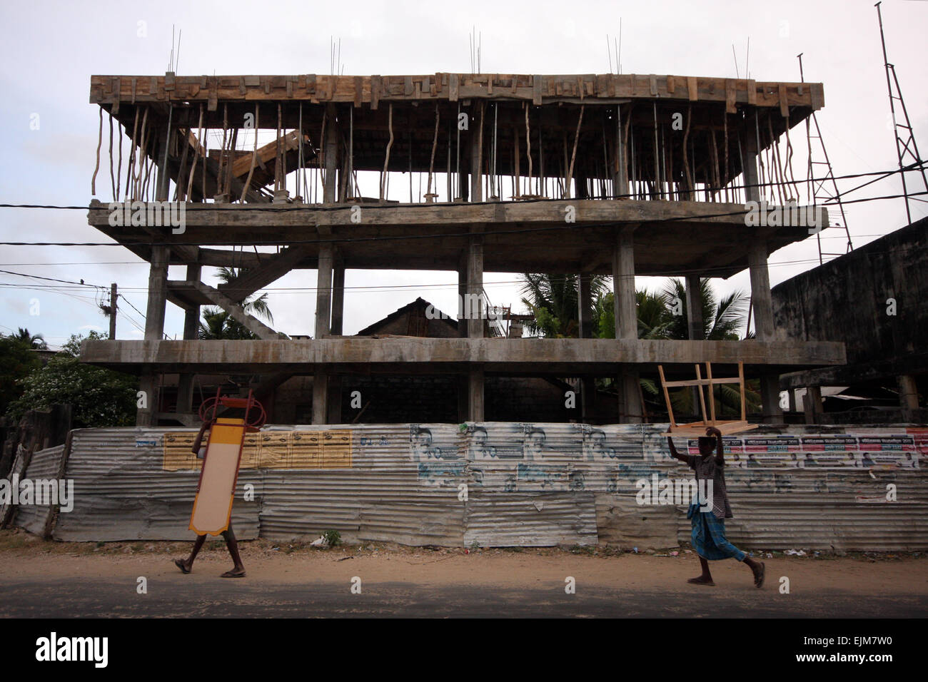 Leute, die Möbel an einem halbgebauten Gebäude vorbeischleppen, Jaffna, Sri Lanka Stockfoto