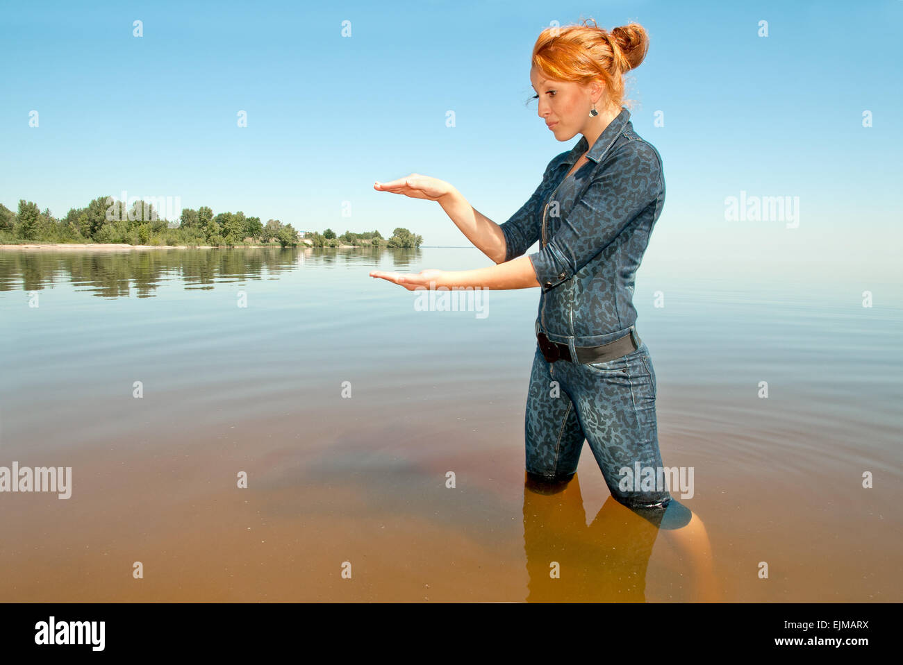 Mädchen mit roten Haaren. Stehen knietief im Wasser, ein imaginäres Objekt zu halten. Stockfoto