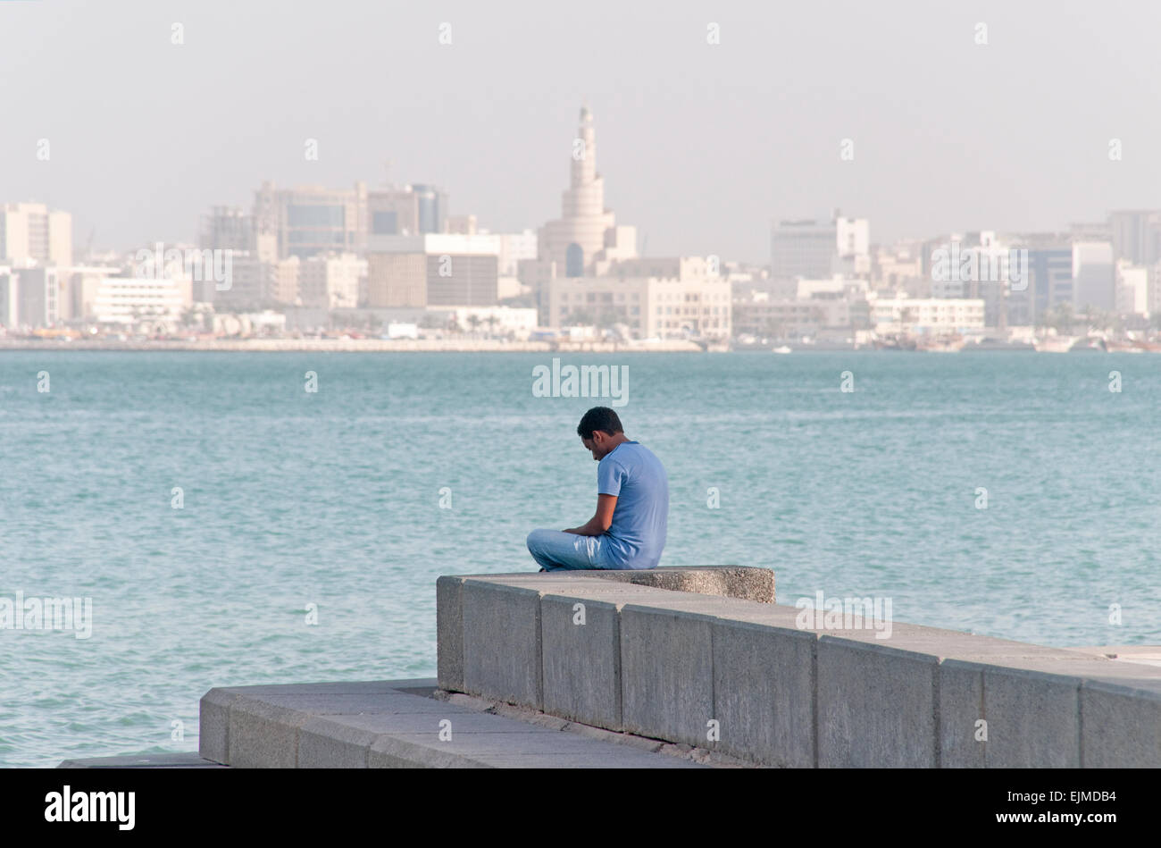 Ein Mann sitzt allein in Doha, Katar, mit dem Stadtbild und den Persischen Golf im Hintergrund. Stockfoto