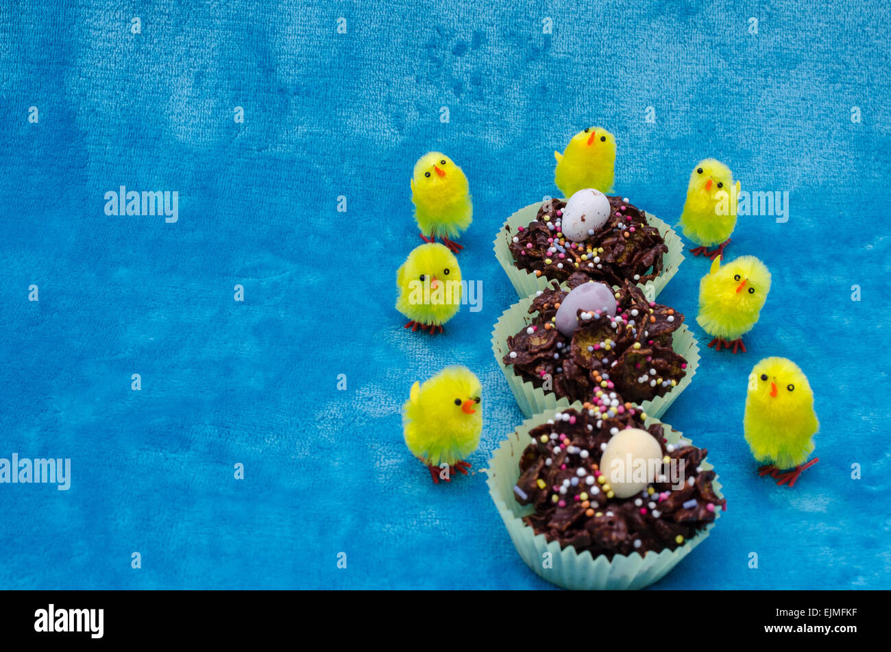 Perfektes Bild für das Osterfest. Drei Cornflakes-Kuchen in einer Reihe sind umgeben von kleinen Küken gelb Spielzeug. Stockfoto