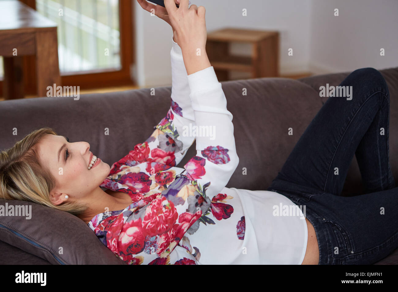 Attraktive Frau sitzt auf der gemütlichen Couch im hellen Wohnzimmer mit einem Anruf Stockfoto