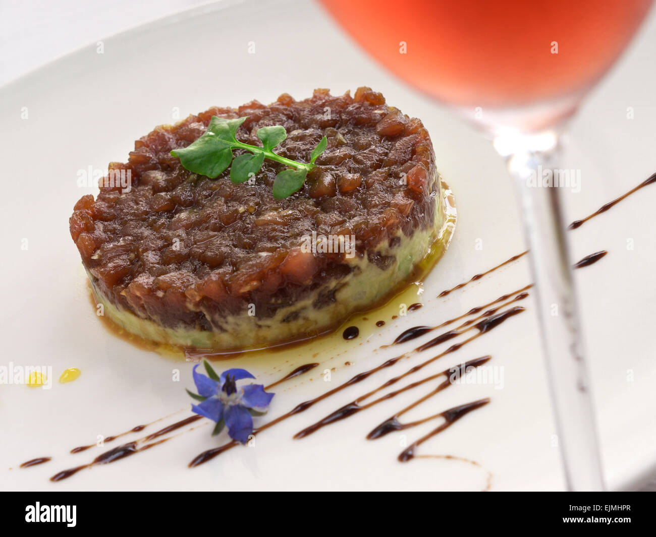 Thunfischtartara-Vorspeise attraktiv auf Restauranttisch im Freien mit einem Glas Rosensekt im Vordergrund Stockfoto