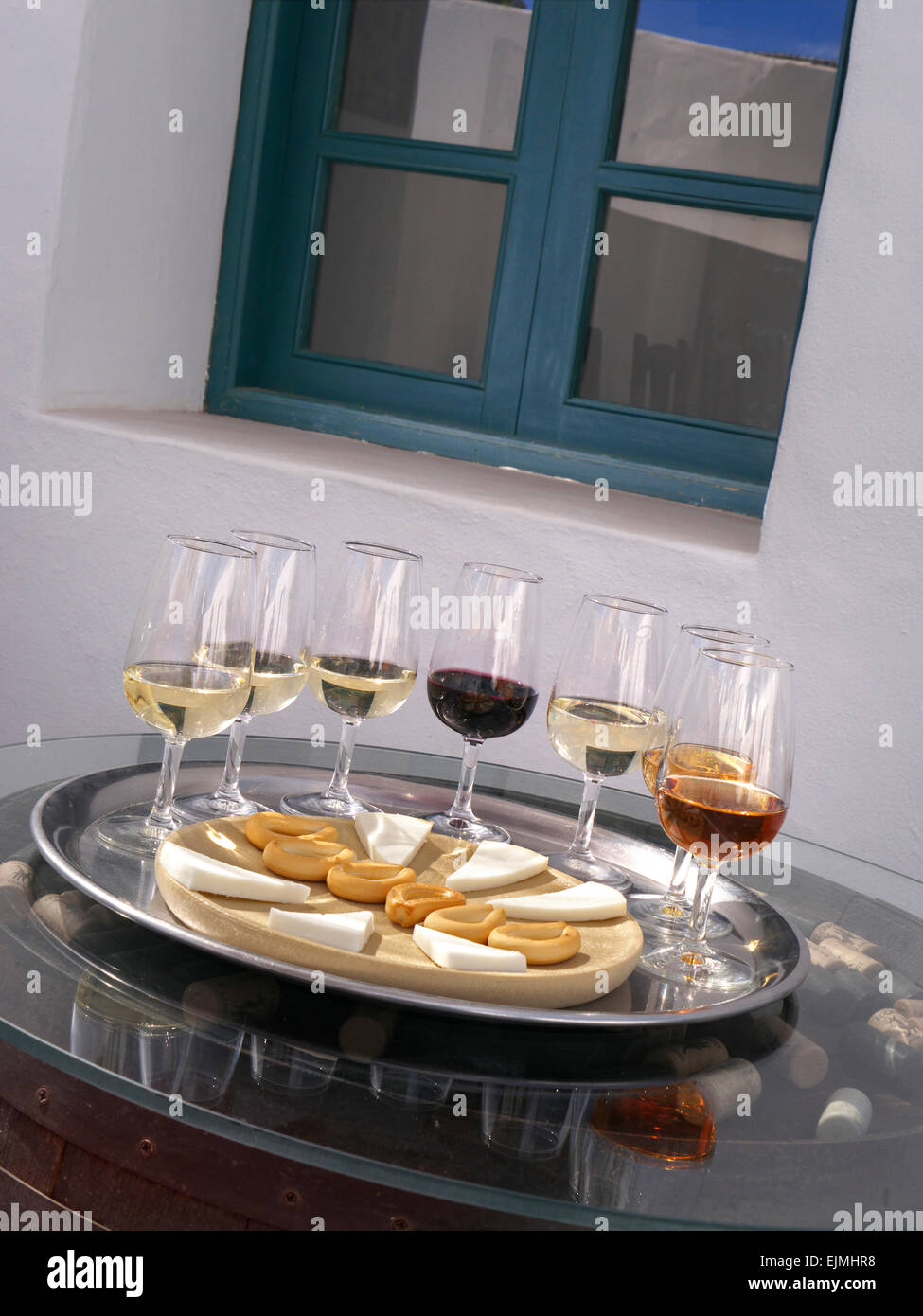 Weinprobe im Freien mit einer Auswahl an Rot- und Weißweinen mit Käse und trockenen Keksen am Fassende mit Korken und Weinbodega dahinter Stockfoto