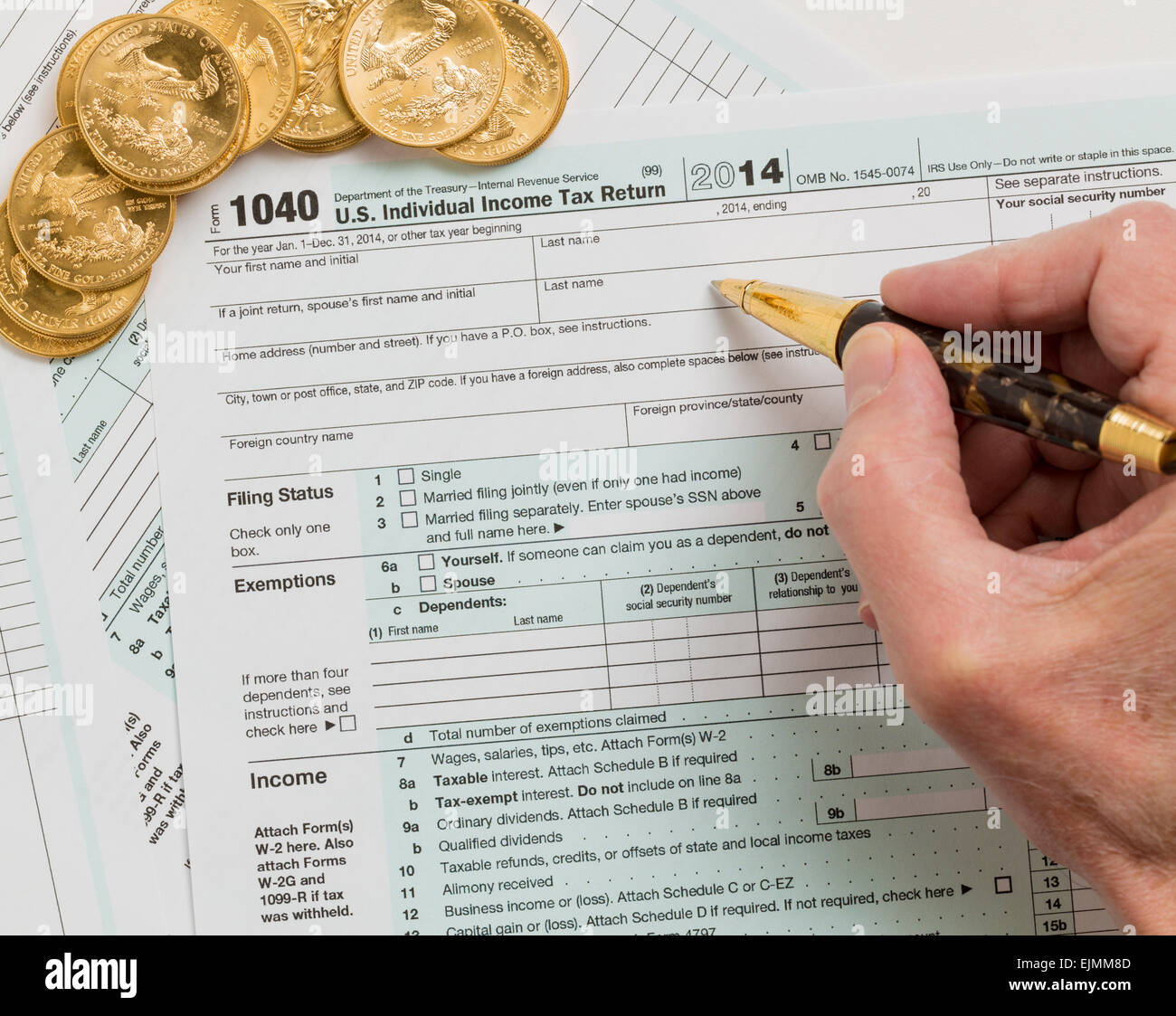 Kaukasische Hand mit Stift und solid gold Eagle-Münzen auf USA tax Form 1040 für Jahr 2014 zur Veranschaulichung Zahlung von Steuern auf Formulare für Stockfoto