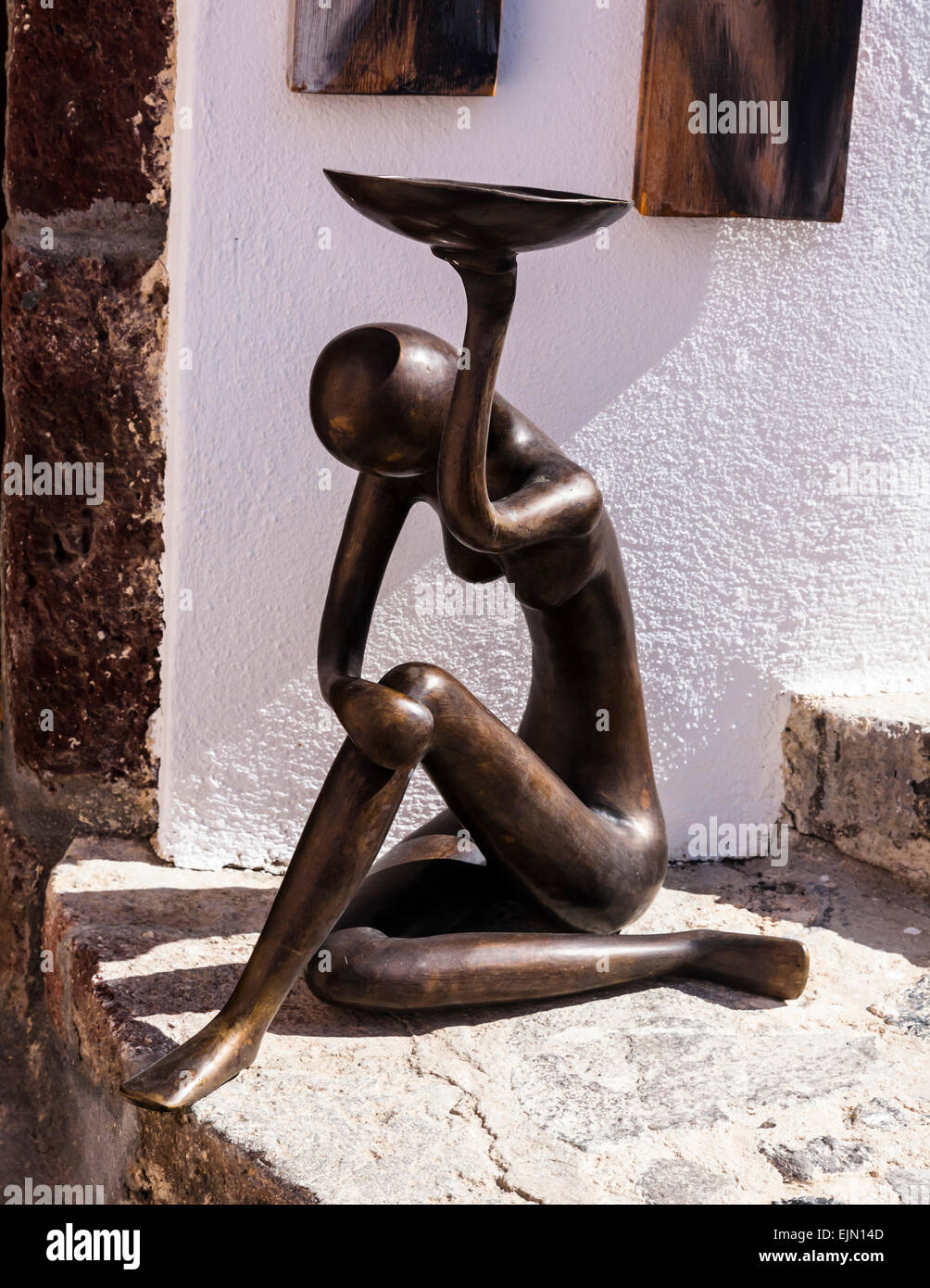 Kleine abstrakte weibliche menschliche Bronzefigur sitzend auf einer Stufe und eine Schüssel hochhalten. Stockfoto