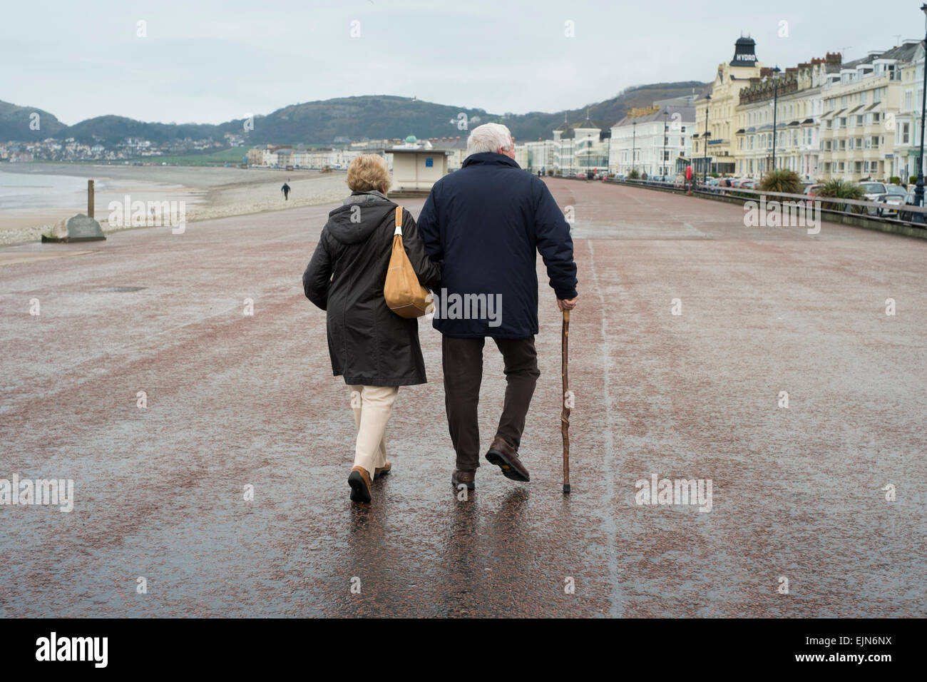 Männliche und weibliche Senioren zu Fuß entlang der Strandpromenade in Llandudno, Wales, im Regen. Stockfoto