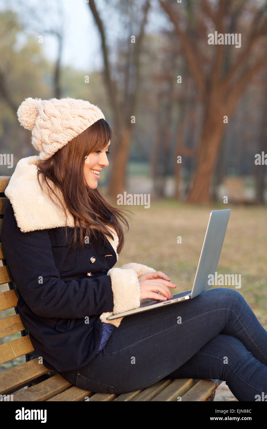 Mädchen sitzen mit Laptop auf Bank im Park im Winter Blick auf dem laptop Stockfoto