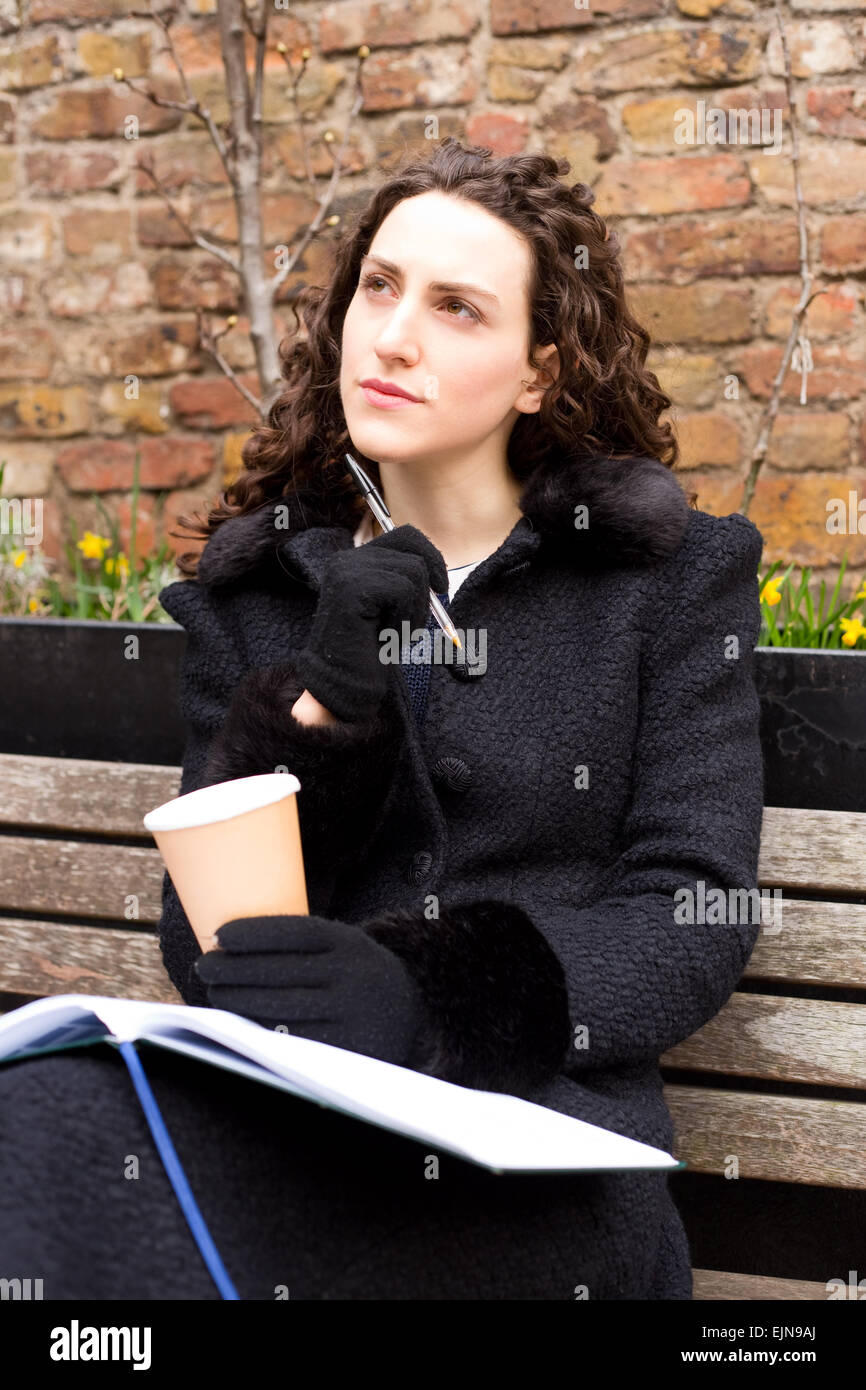 eine nachdenkliche junge Frau mit einem Kaffee und Tagebuch Stockfoto