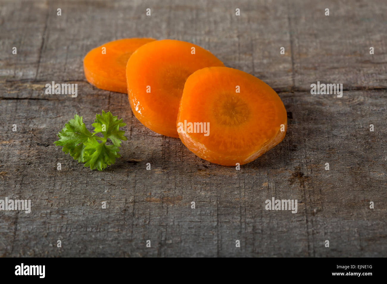 In Scheiben geschnitten zum Kochen Karotten auf ein Schneidebrett und Petersilie auf einem hölzernen Hintergrund Stockfoto