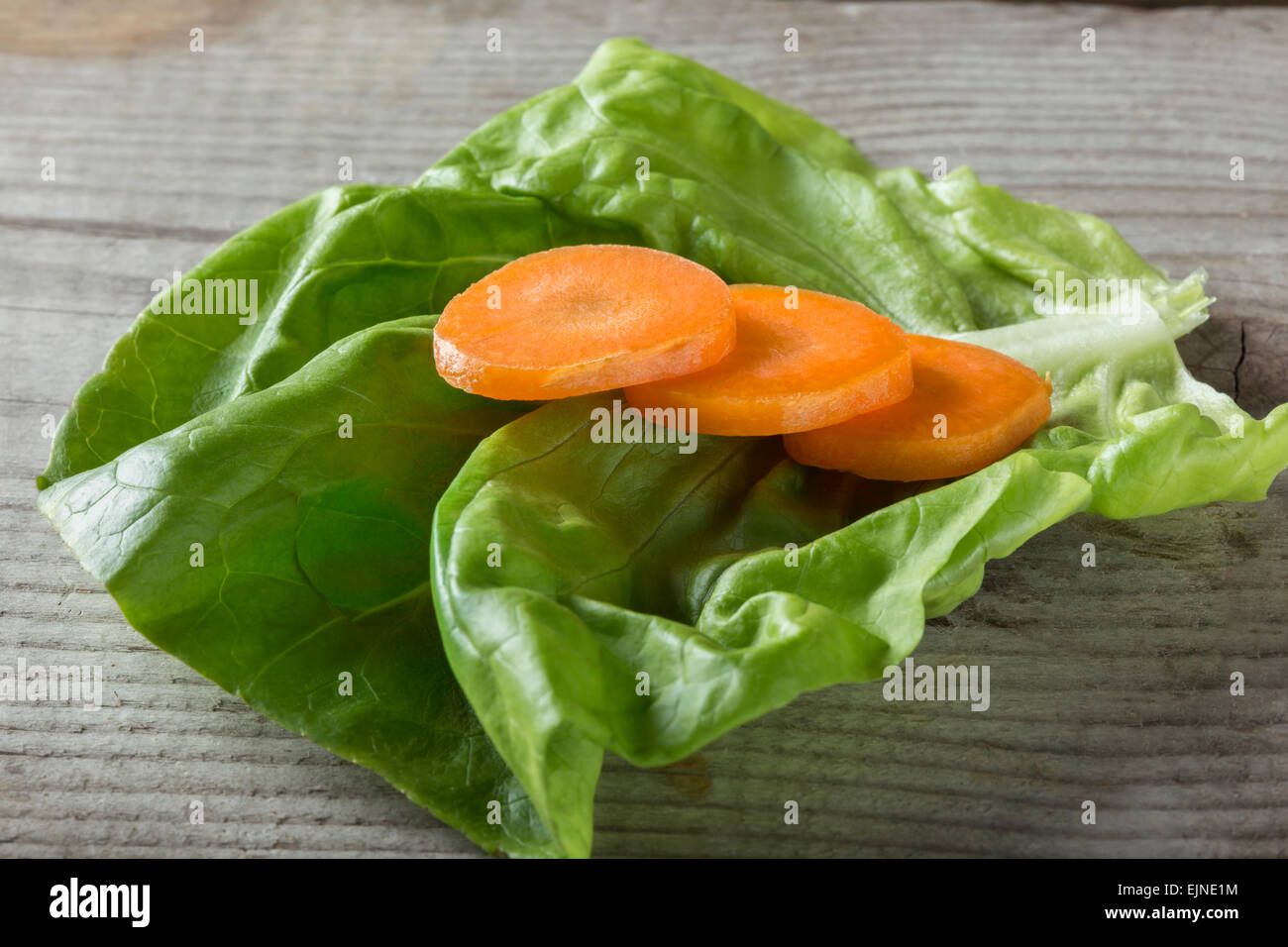 Schuss von geschnittene Karotten auf einem Blatt Salat über hölzerne Hintergrund hautnah Stockfoto