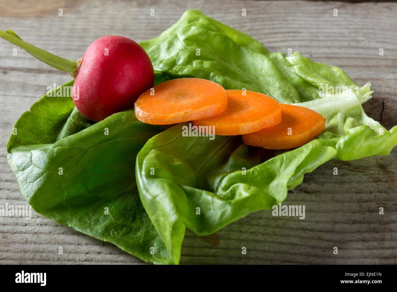 Schuss von Rettich und geschnittene Karotten auf einem Blatt Salat über hölzerne Hintergrund hautnah Stockfoto