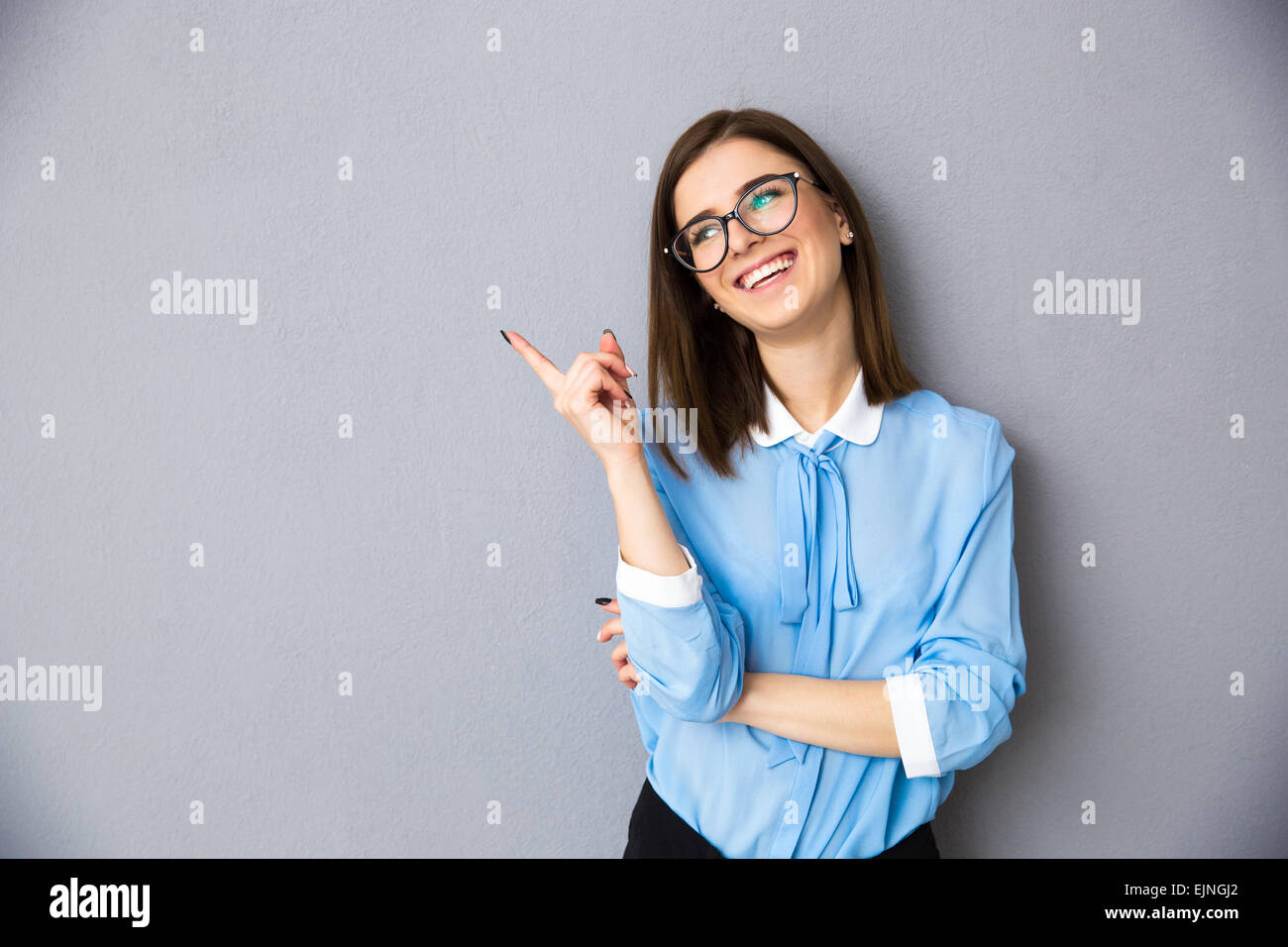 Fröhliche Geschäftsfrau entfernt über grauen Hintergrund zeigend. Im blauen Hemd und Brille tragen. Wegschauen Stockfoto