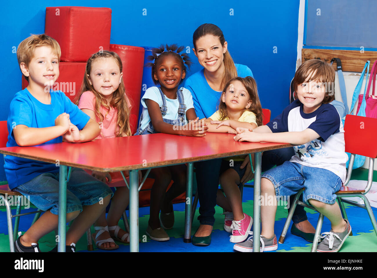Glückliche Kinder sitzen zusammen mit Kindergärtnerin am Tisch im kindergarten Stockfoto