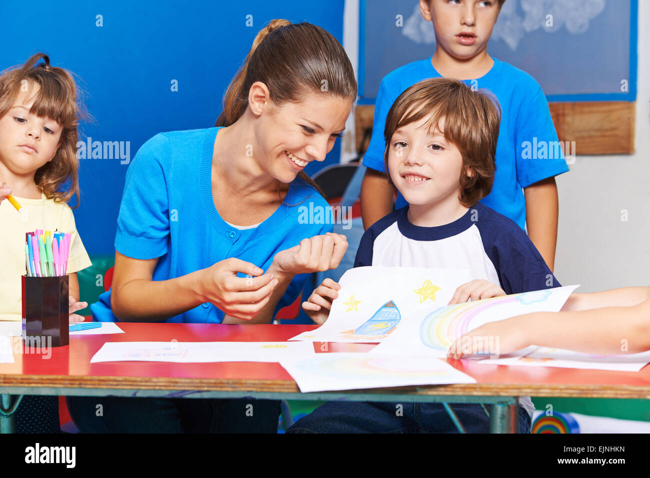 Glückliche Kinder zeichnen mit lächelnden Kindergärtnerin im kindergarten Stockfoto